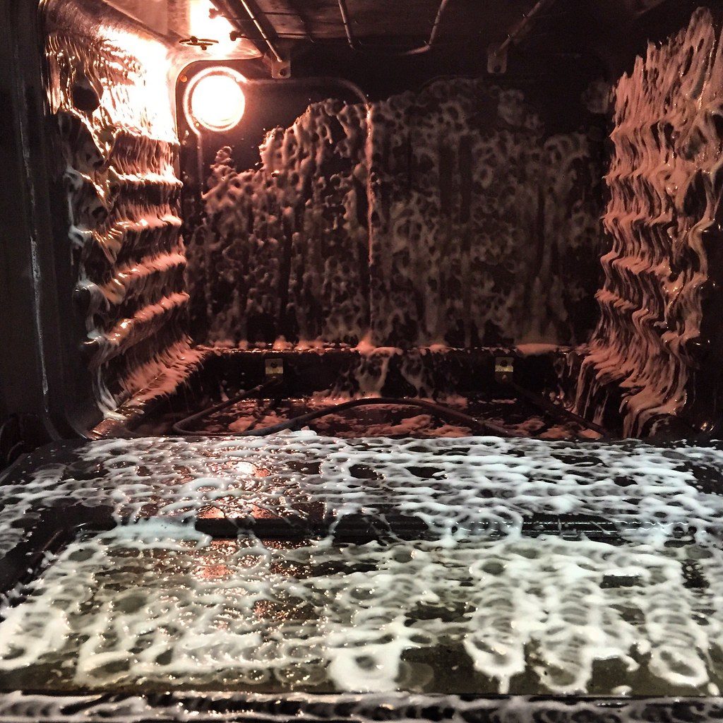 The inside of an oven coated in cleaning foam, lit by the oven lamp